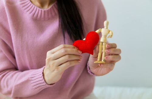 Eine Frau hält ein rotes Stoffherz in der einen und eine kleine Holzfigur in der anderen Hand.