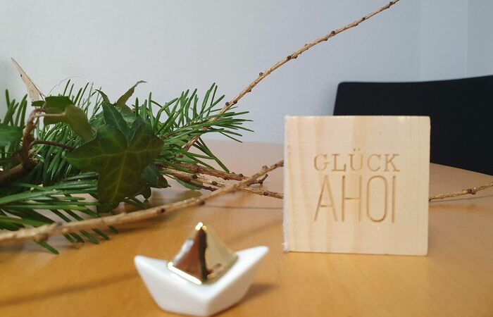 Eine kleine Skulptur eines Bootes steht vor einem Holzschild mit dem Aufdruck "Glück Ahoi"