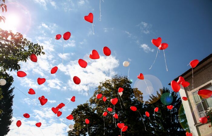 Viele rote bunte Luftballons in Herzform steigen in den Himmel.