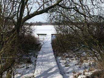 Ein schneebedeckter Steg führt auf einen See hinaus.